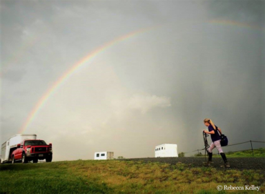 student getting ready for horse show carries tack to trailer parked under a rainbow
