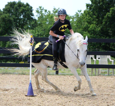 eager student in Batman costume races pony around mounted games bending pole